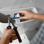Toilet Tank Not Filling. Image of someone with a wrench fixing a part inside a toilet tank.